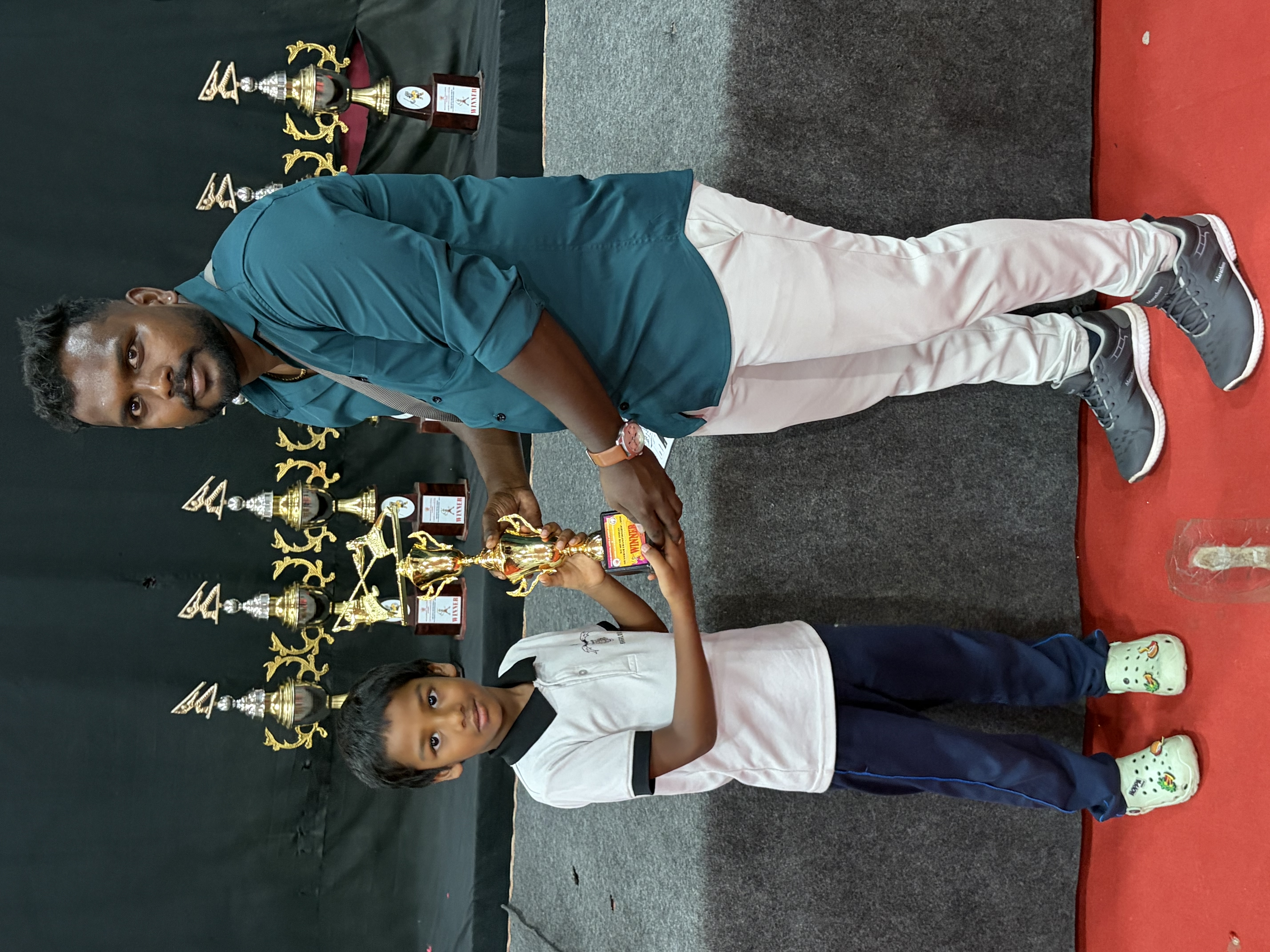 Prithvi receiving his trophy from his coach at the prize table lined with cups