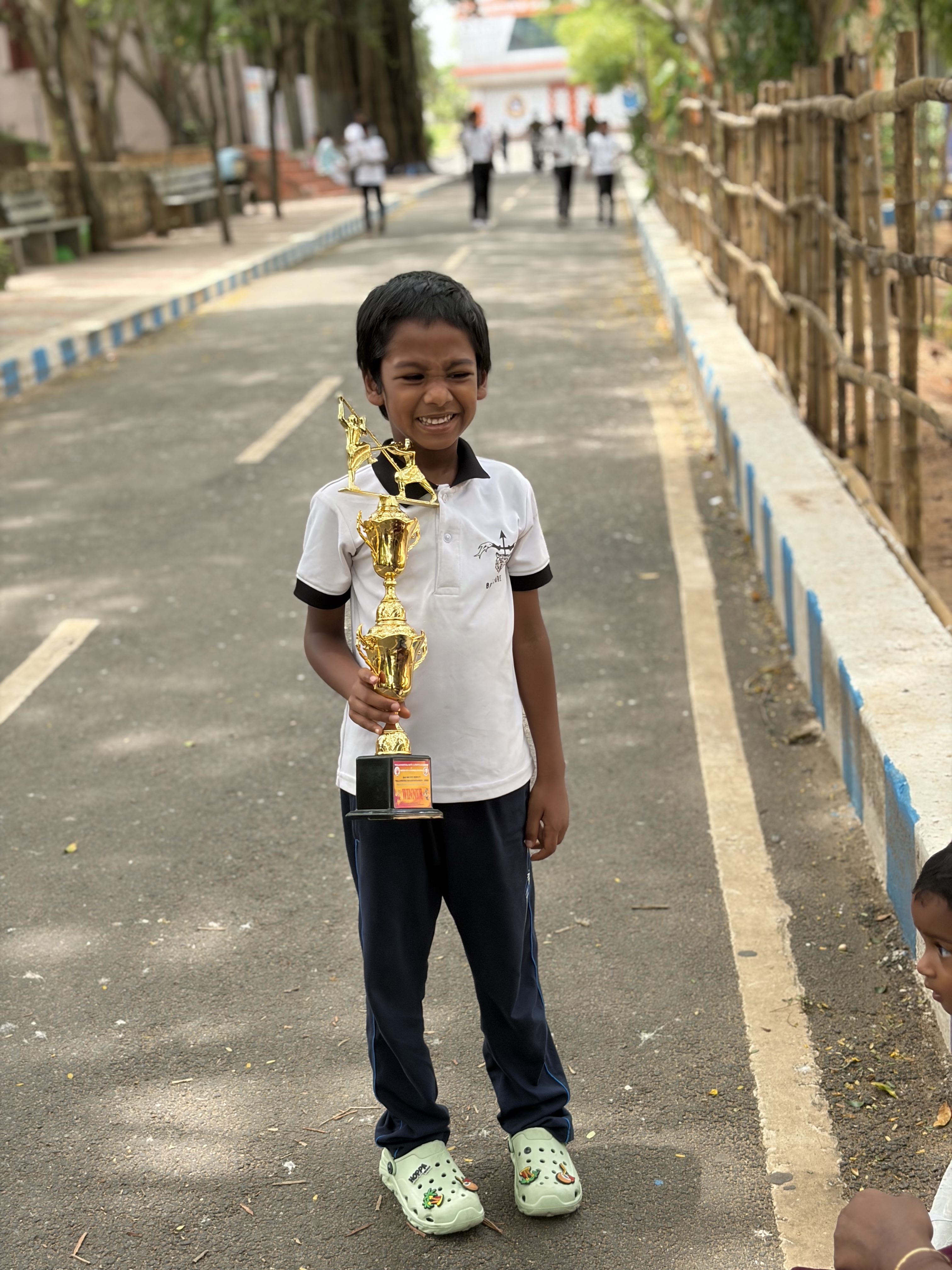 Prithvi grinning on the tree-lined path holding his winner's trophy