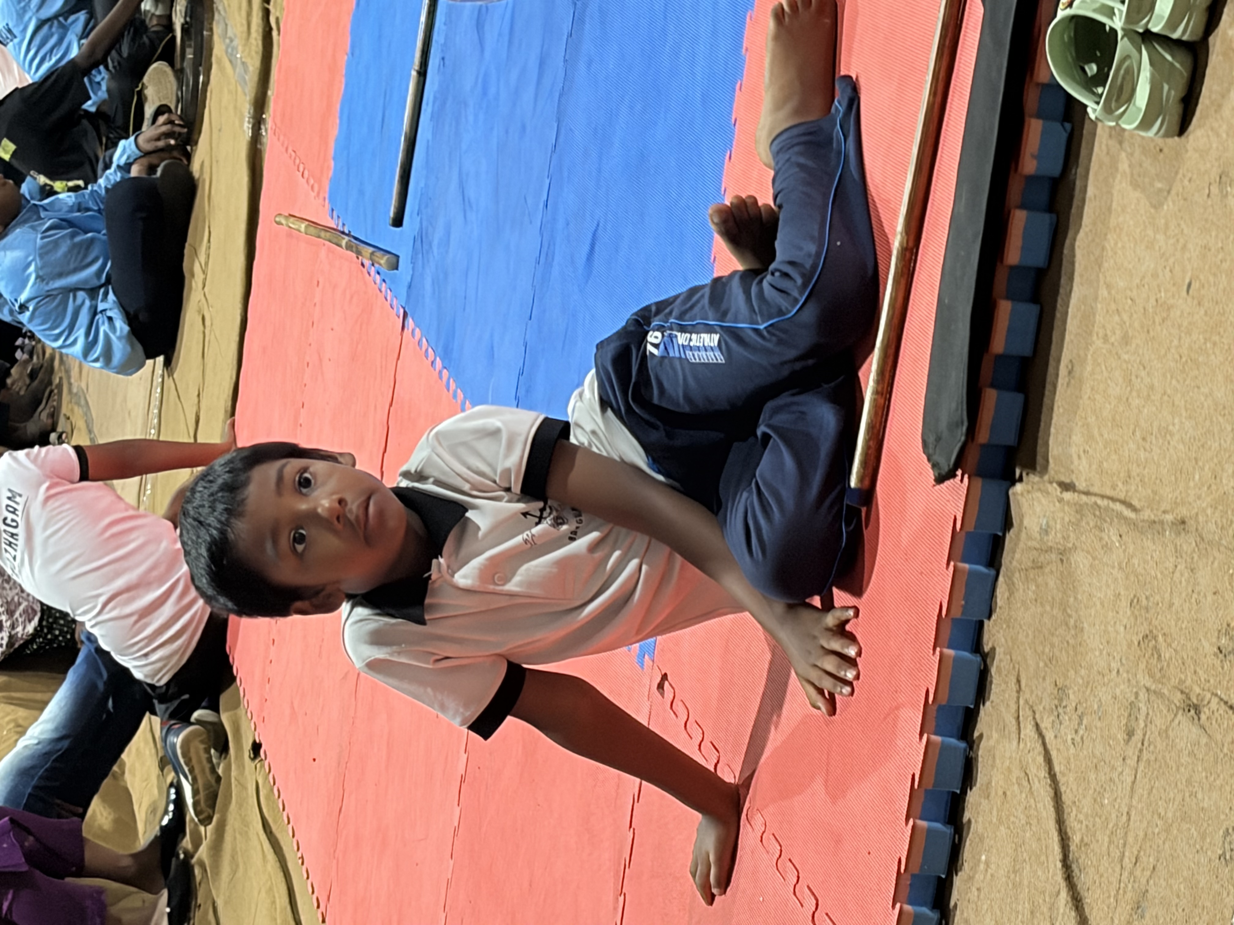 Prithvi in a low, grounded stance on the mat, stick beside him