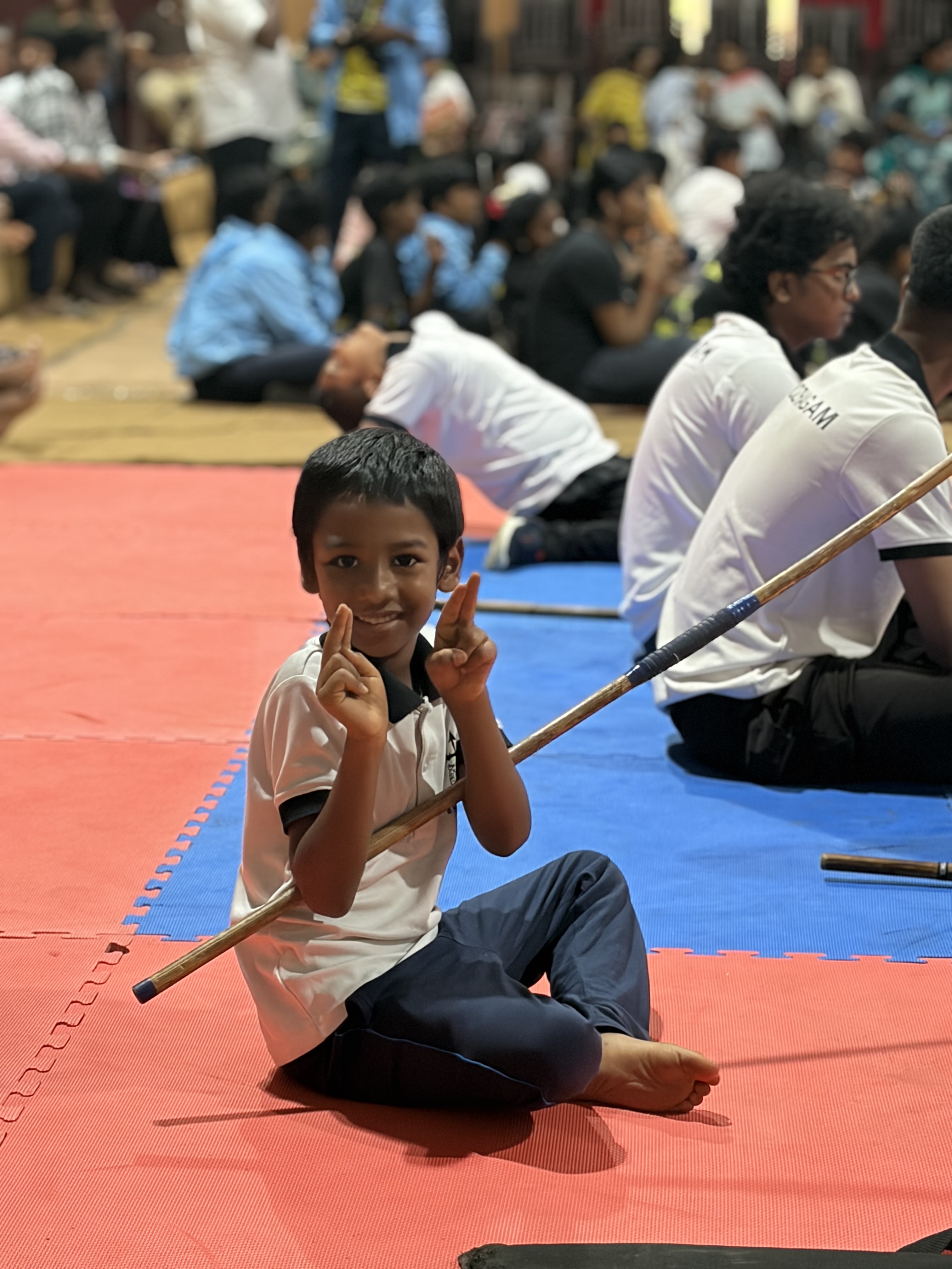 Prithvi smiling, holding the Silambam stick across, fingers raised