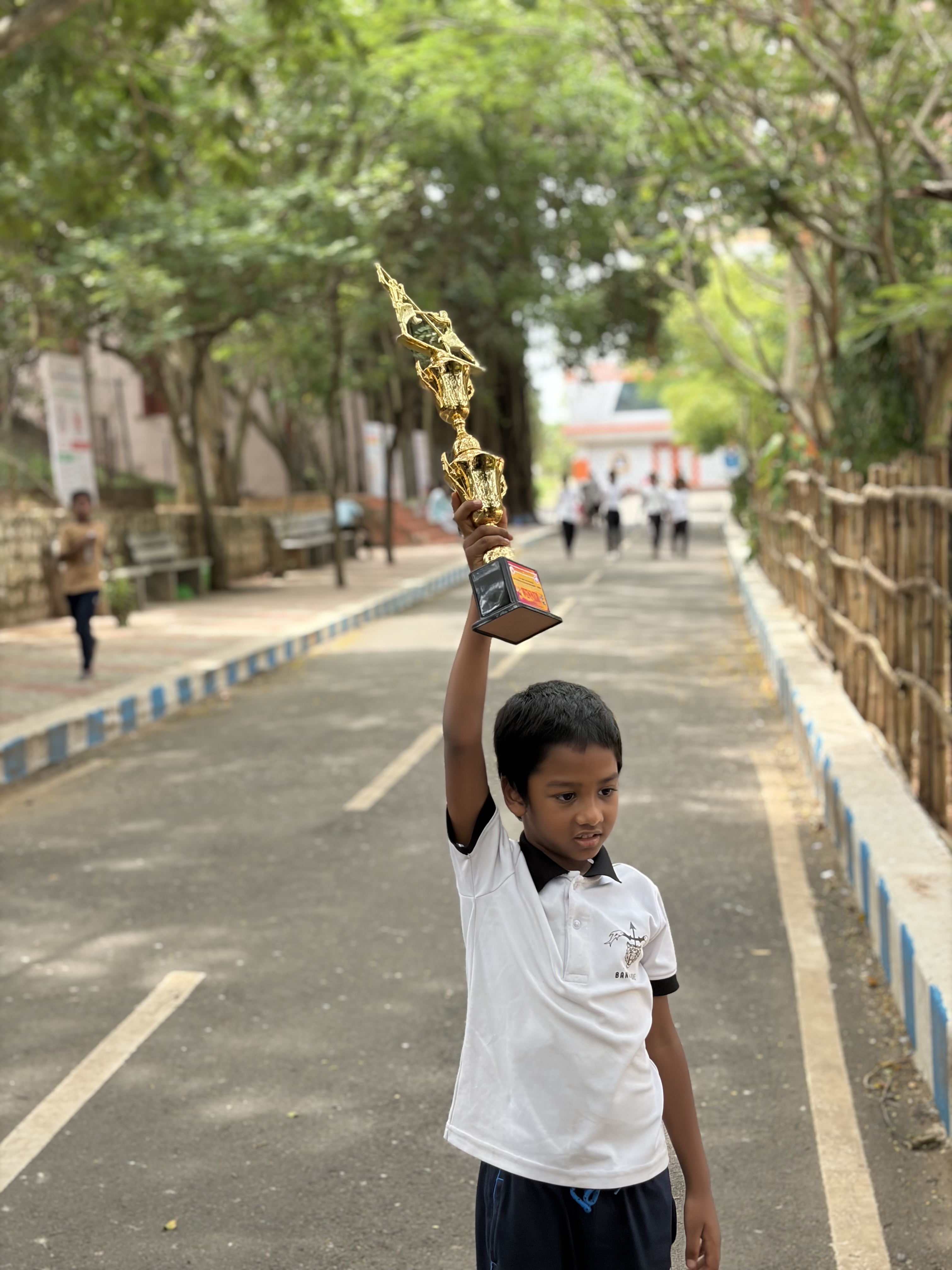 Prithvi holding his trophy high above his head on a tree-lined path